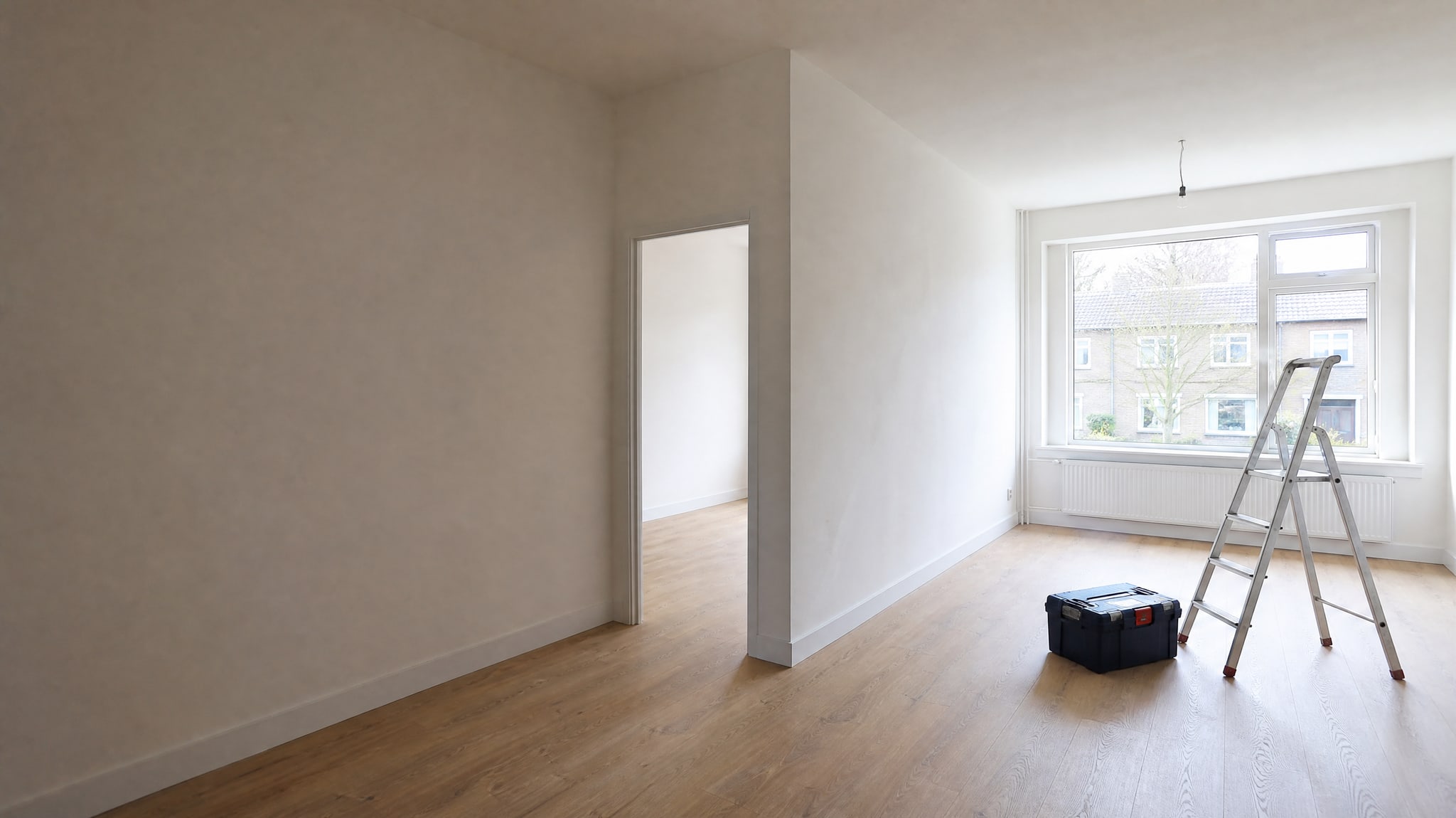 Lichte woonkamer na een verbouwing, met strak gestucte wanden, een nieuwe tussenwand en een trap en gereedschapskist bij het raam